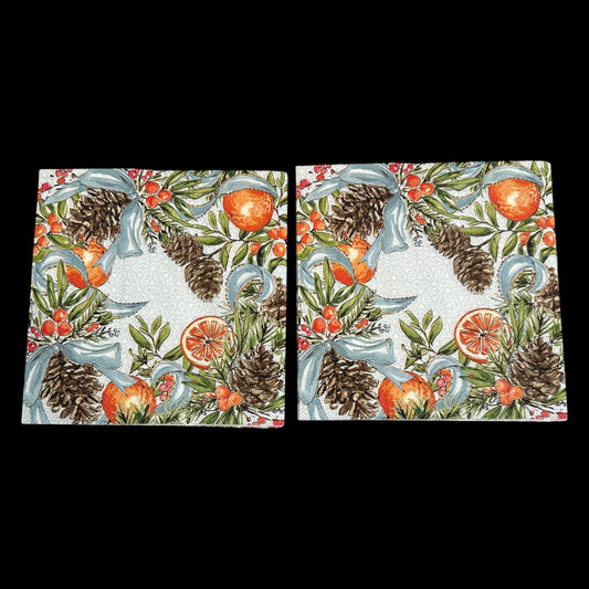 Two Luncheon size decoupage napkin featuring pinecones, oranges, citrus slices, red berries, and blue ribbons on a white patterned background for holiday crafts.