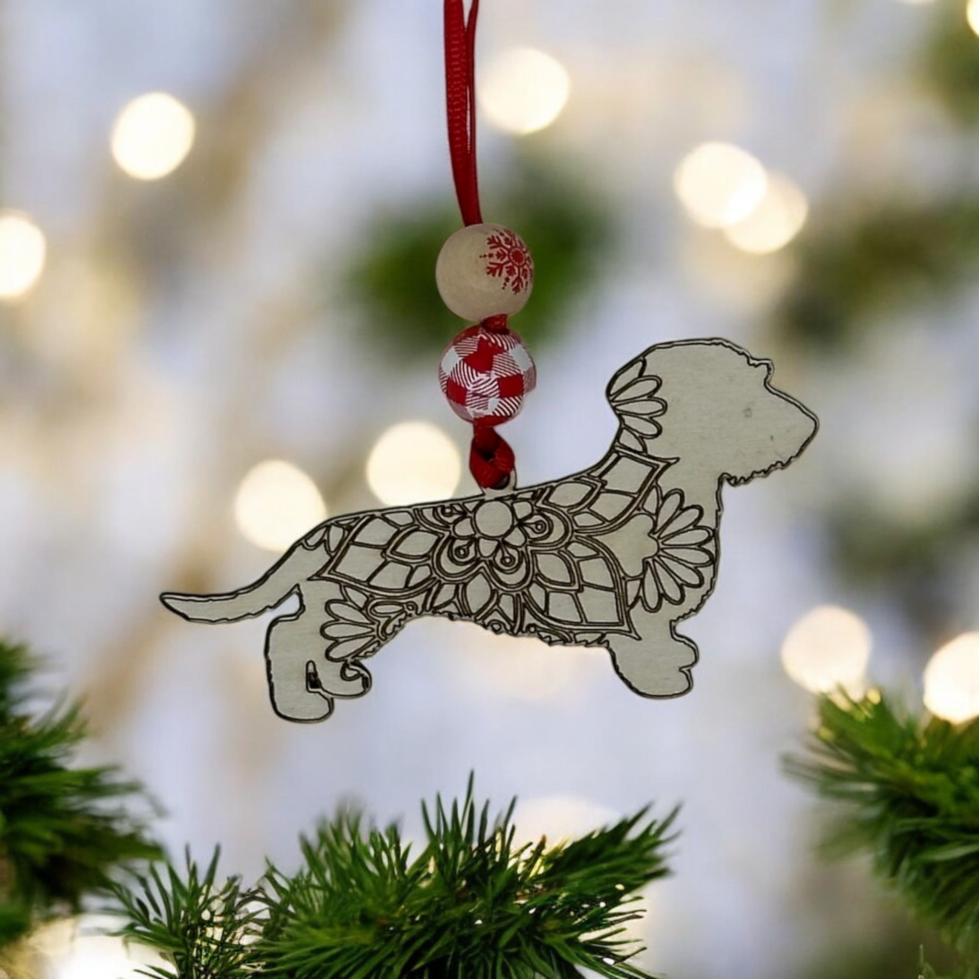Handcrafted wooden wire-haired Dachshund ornament with mandala design hanging on a Christmas tree branch.