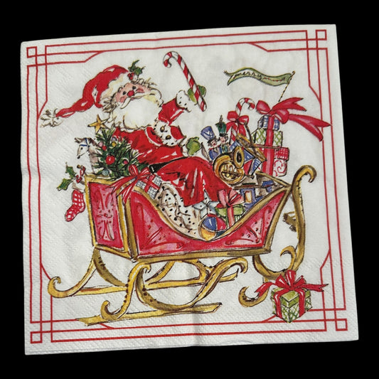 Luncheon size decoupage napkin featuring Santa Claus in a red sleigh filled with gifts, candy canes, and holly, bordered in red and gold for Christmas crafts.