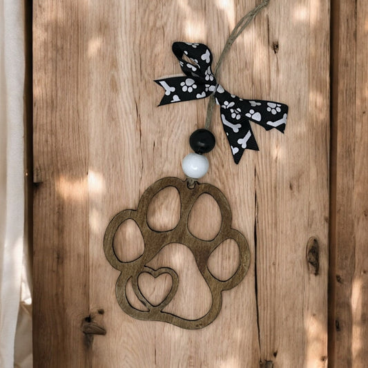 wooden paw print with a heart ornament on a jute cord with two wooden beads and a black ribbon bow with white paw prints and dog bones