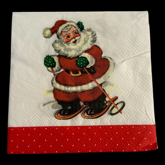 Close-up of a cocktail napkin featuring a retro Santa Claus skiing with green mittens and a red suit, set against a white background with a red polka-dot border.