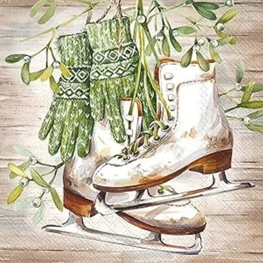 Close-up of a winter cocktail napkin featuring watercolor white vintage ice skates and green mittens hanging with mistletoe on a rustic wooden background.