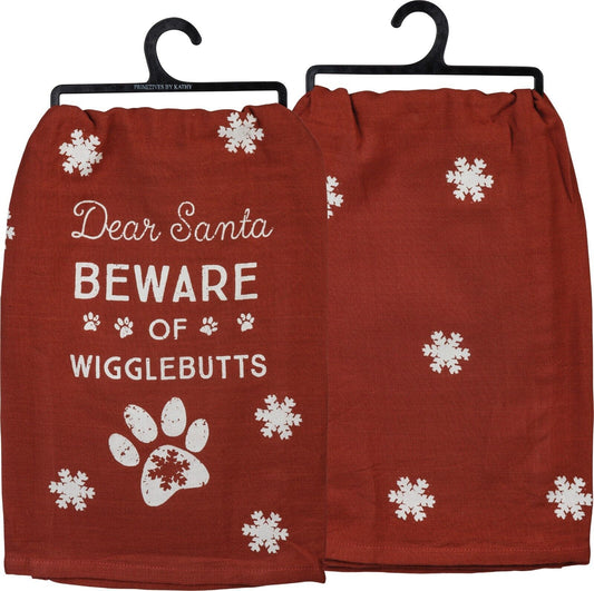 a red kitchen tea towel with white snowflakes that says Dear Santa BEWARE of Wigglebutts